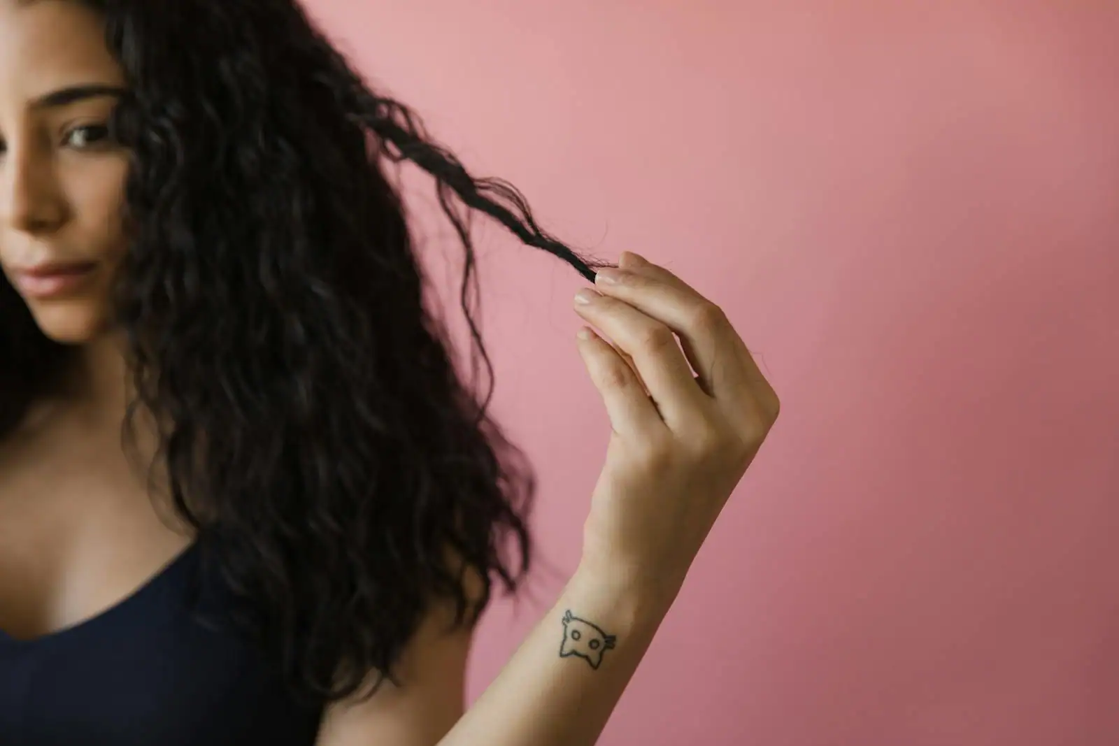Femme aux cheveux longs et brillants replaçant doucement une mèche derrière son oreille, geste de soin et de séduction