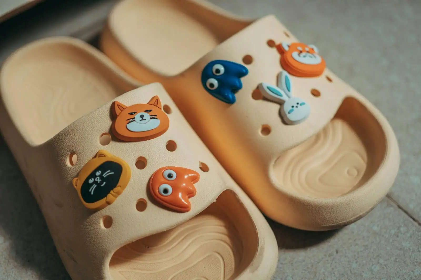 Breloques décoratives en forme d'animaux clipsées dans les trous d'une paire de sabots en mousse beige.