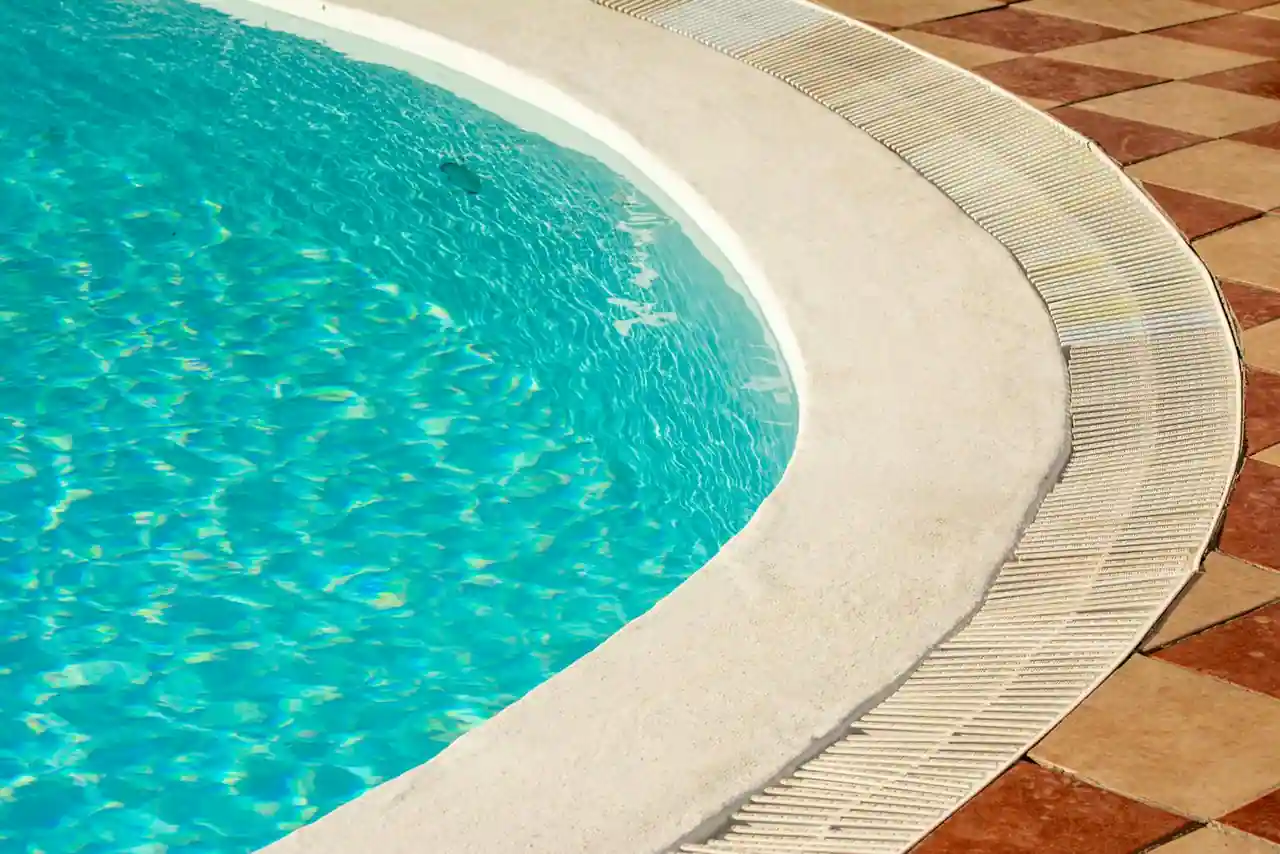 Bord d'une piscine extérieure à l'eau turquoise, avec margelle claire et terrasse carrelée sous le soleil