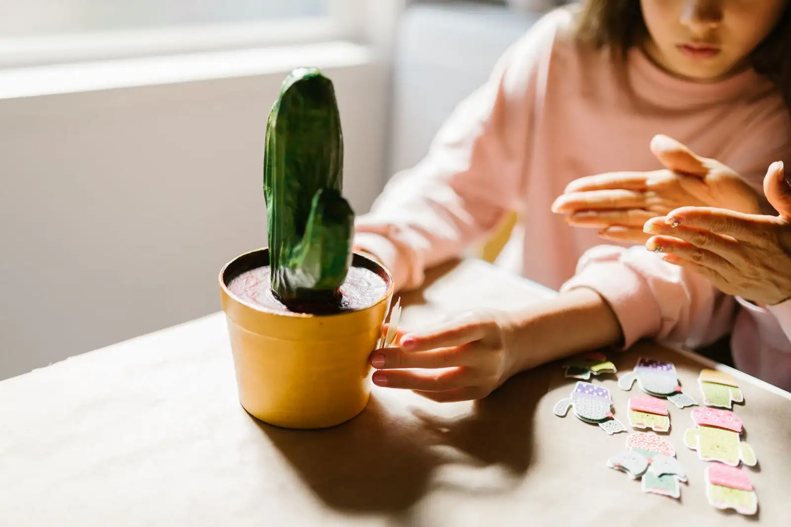 Enfant et adulte réalisant une activité manuelle sur une table, avec un pot décoré et des découpes en papier