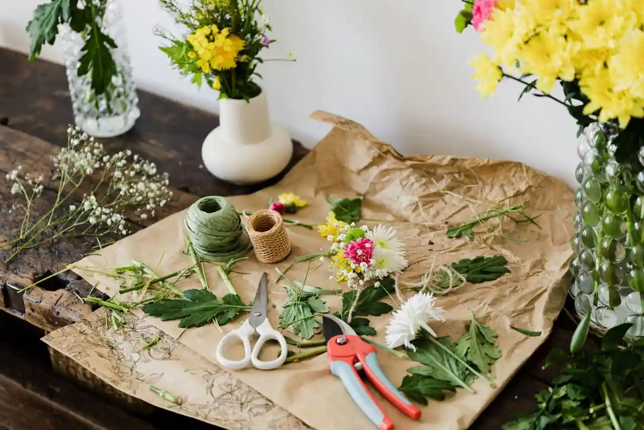 Table de loisirs créatifs au printemps : fleurs fraîches, papier coloré, ciseaux et couronne de feuillage en cours de fabrication