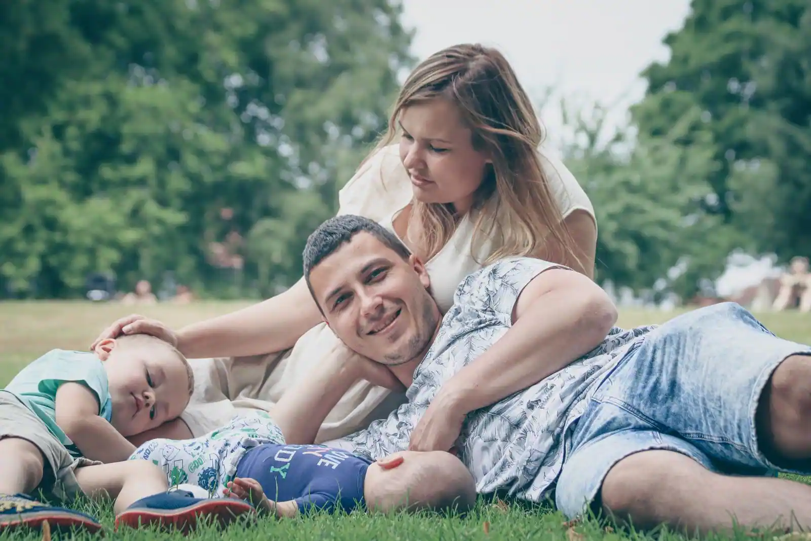 Jeunes parents et leurs enfants allongés dans l'herbe d'un parc, illustrant la vie de famille