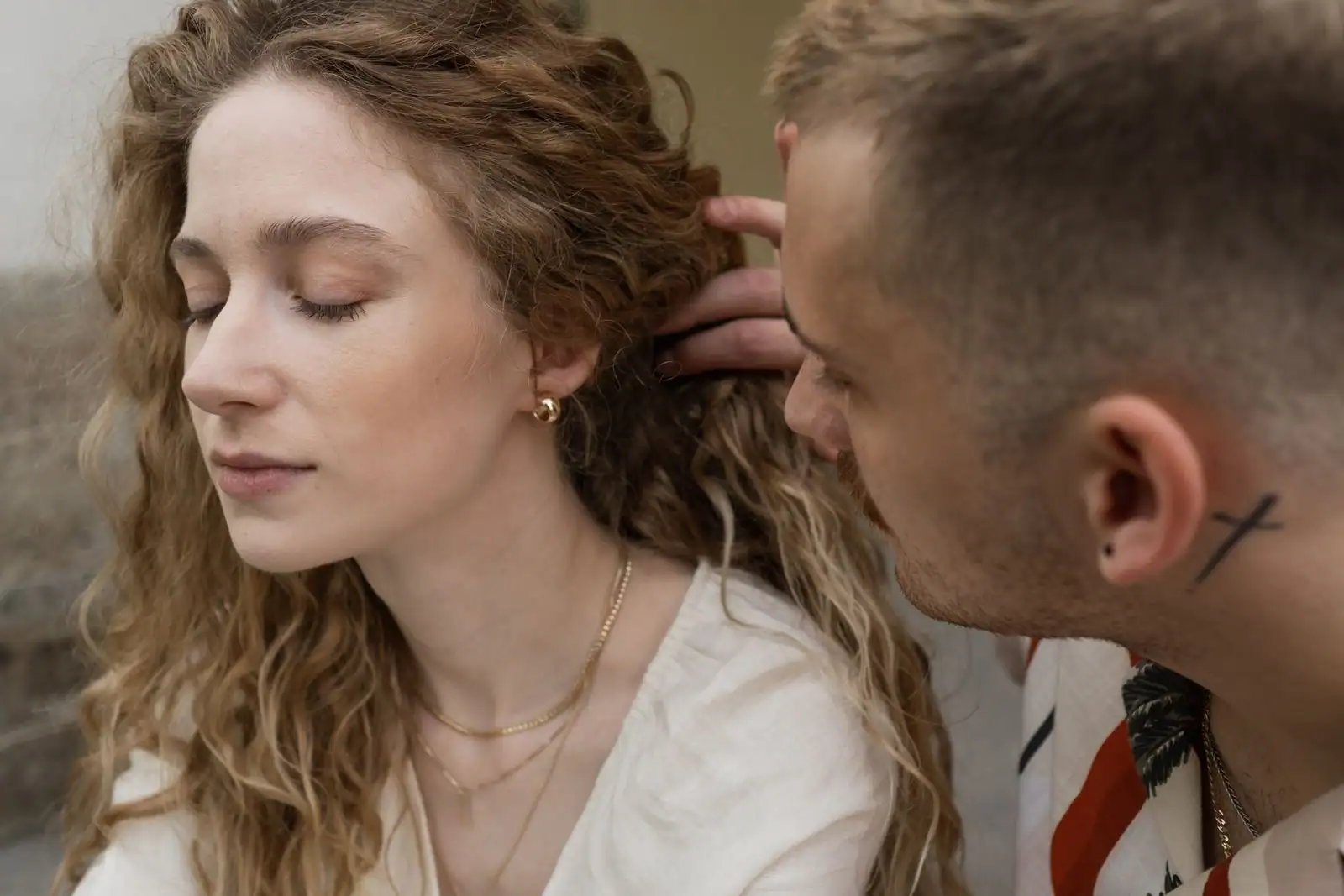 Un homme tout proche glisse la main dans les cheveux bouclés d'une femme aux yeux fermés