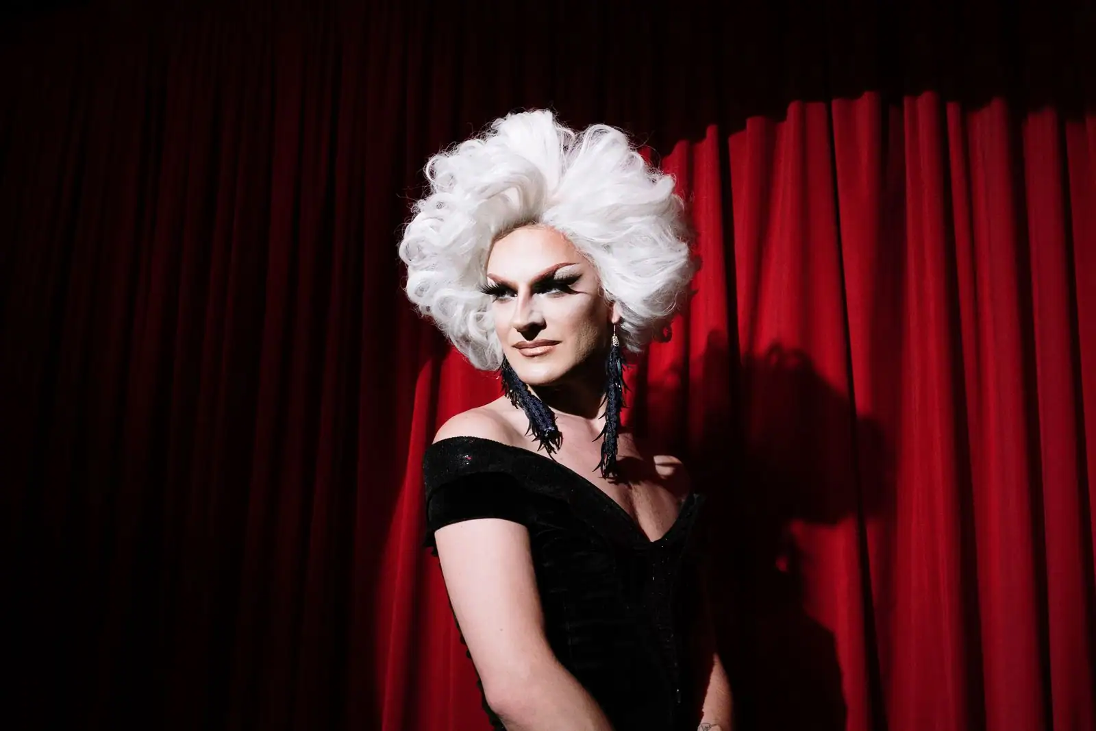 Artiste drag en tenue de scène et maquillage spectaculaire sous les projecteurs.