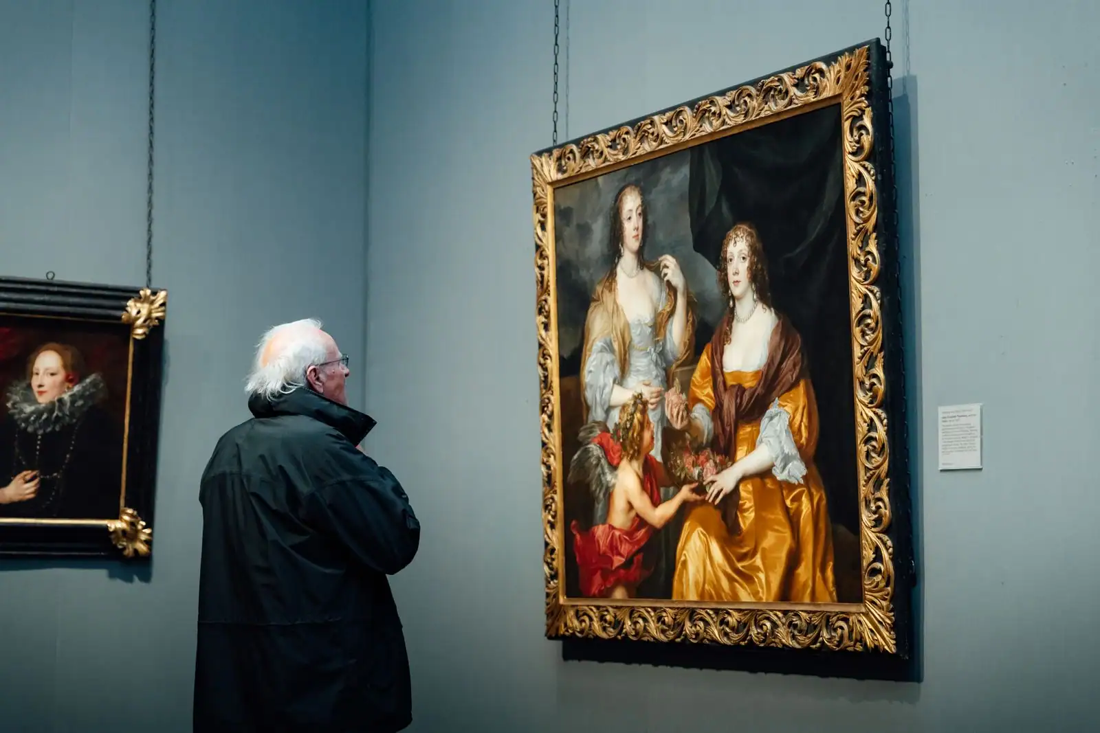 Un visiteur observe un grand tableau classique au cadre doré dans une salle de musée.