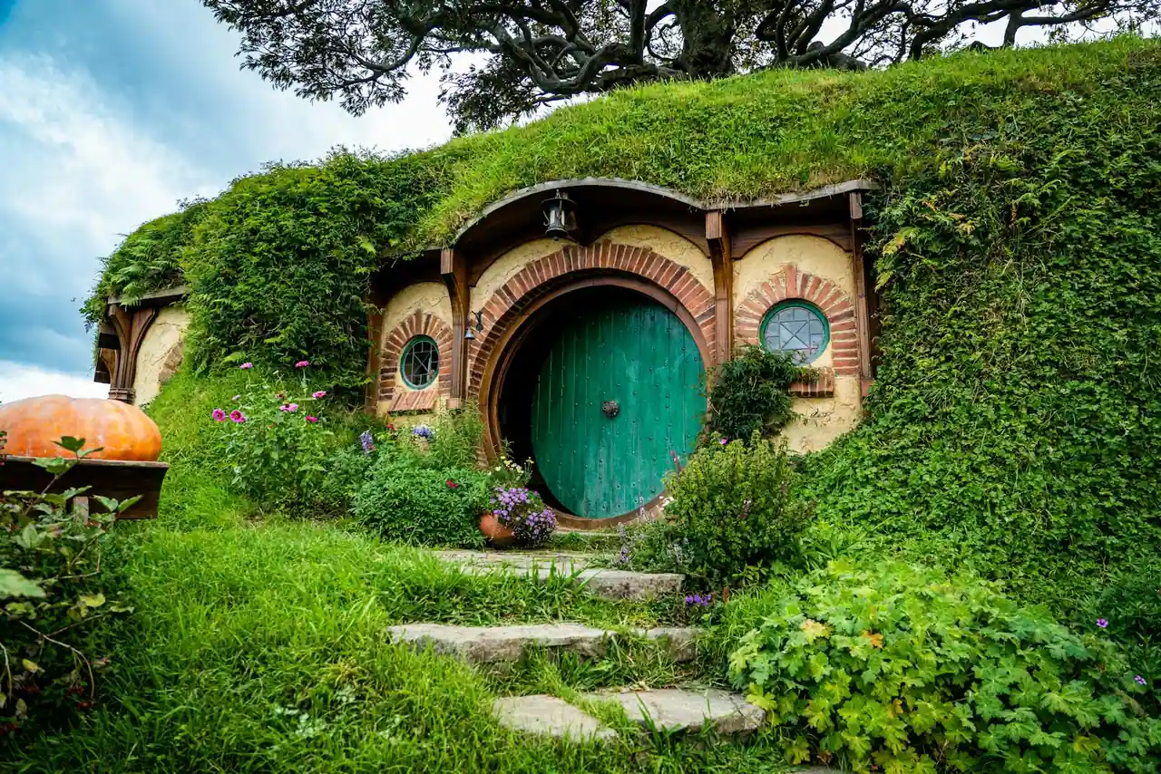 Maison de hobbit ronde adossée à une colline verte, avec sa porte ronde et son toit couvert d'herbe