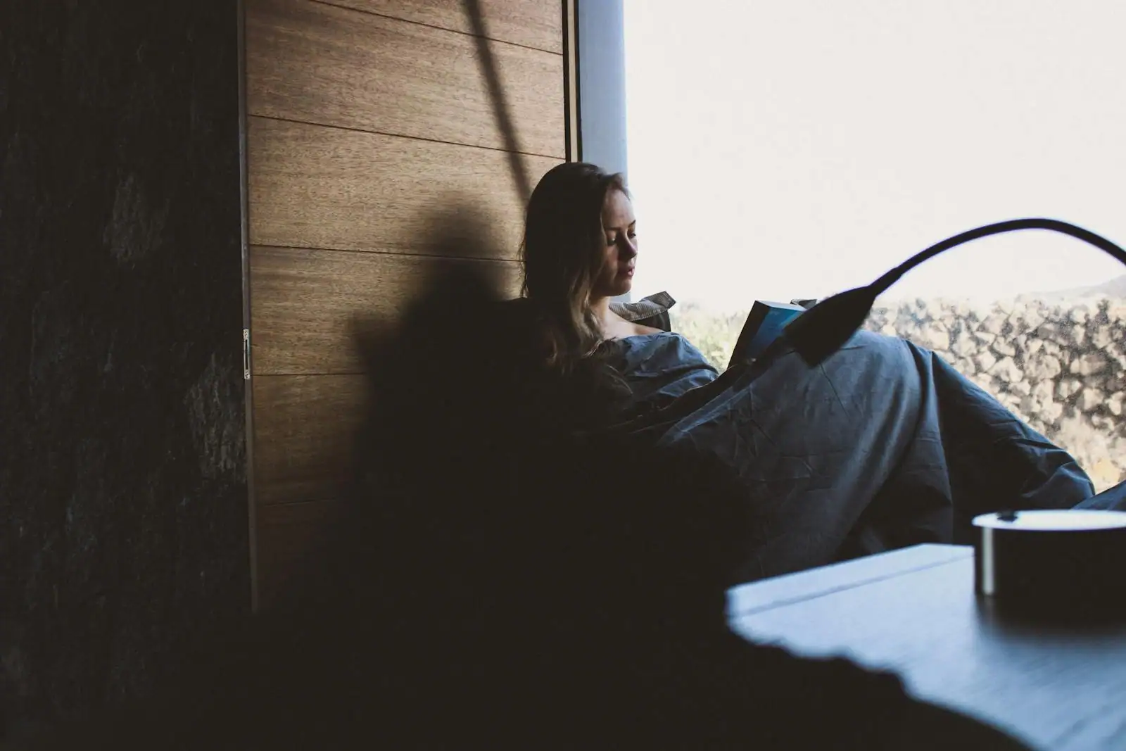 Personne lisant un livre dans un coin calme avec une tasse de thé, lumière douce