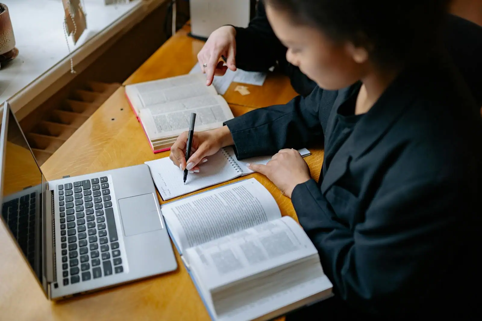 Personne lisant des livres ouverts et prenant des notes dans un carnet sur un bureau