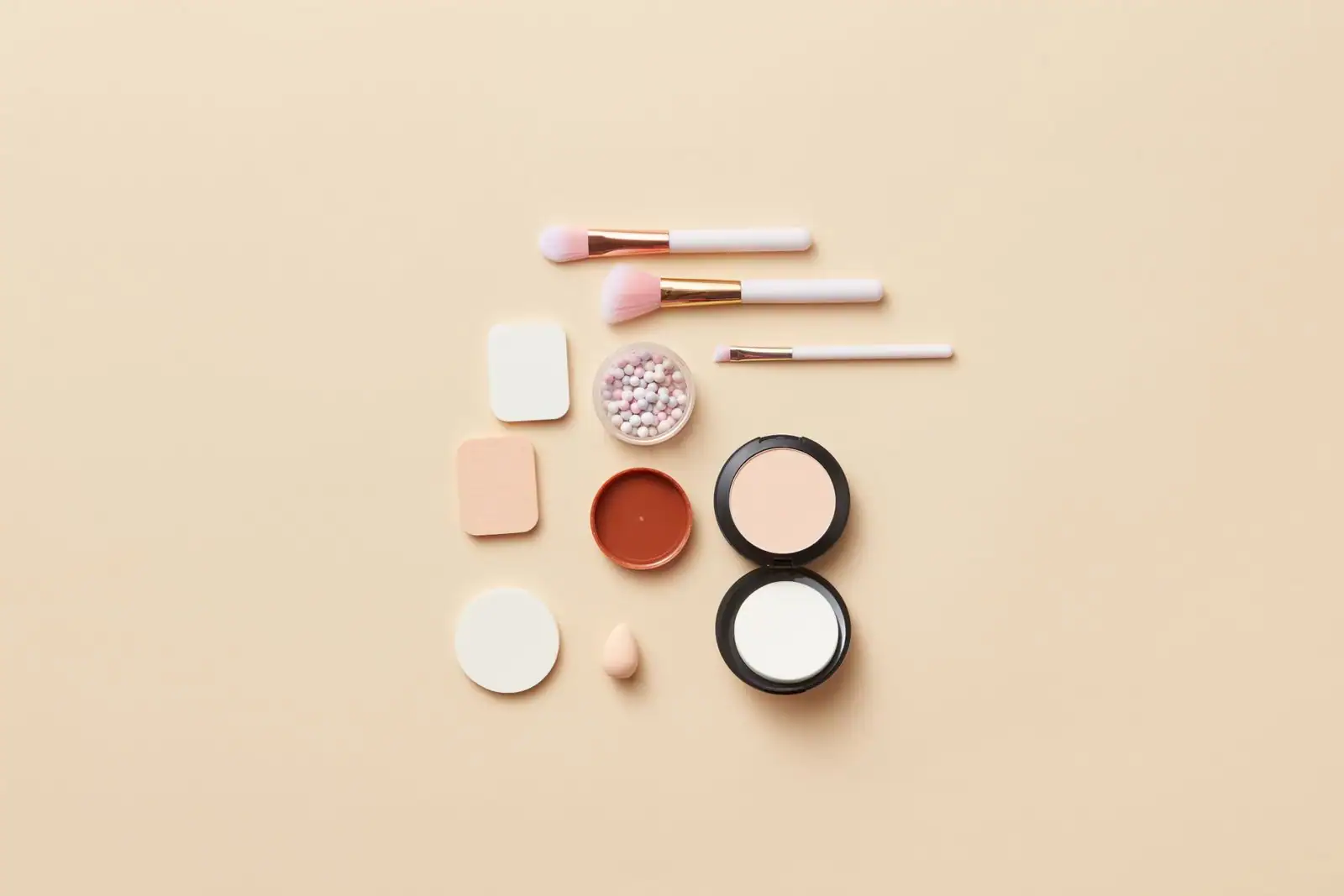 Pinceaux et produits de maquillage disposés à plat sur un fond clair