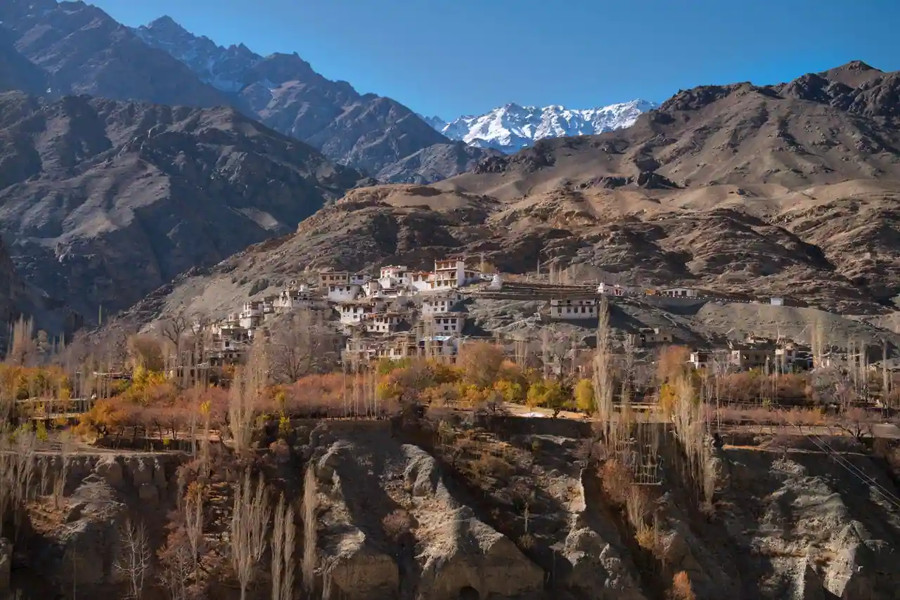 Village de pierre accroché à des montagnes arides, sous des sommets enneigés