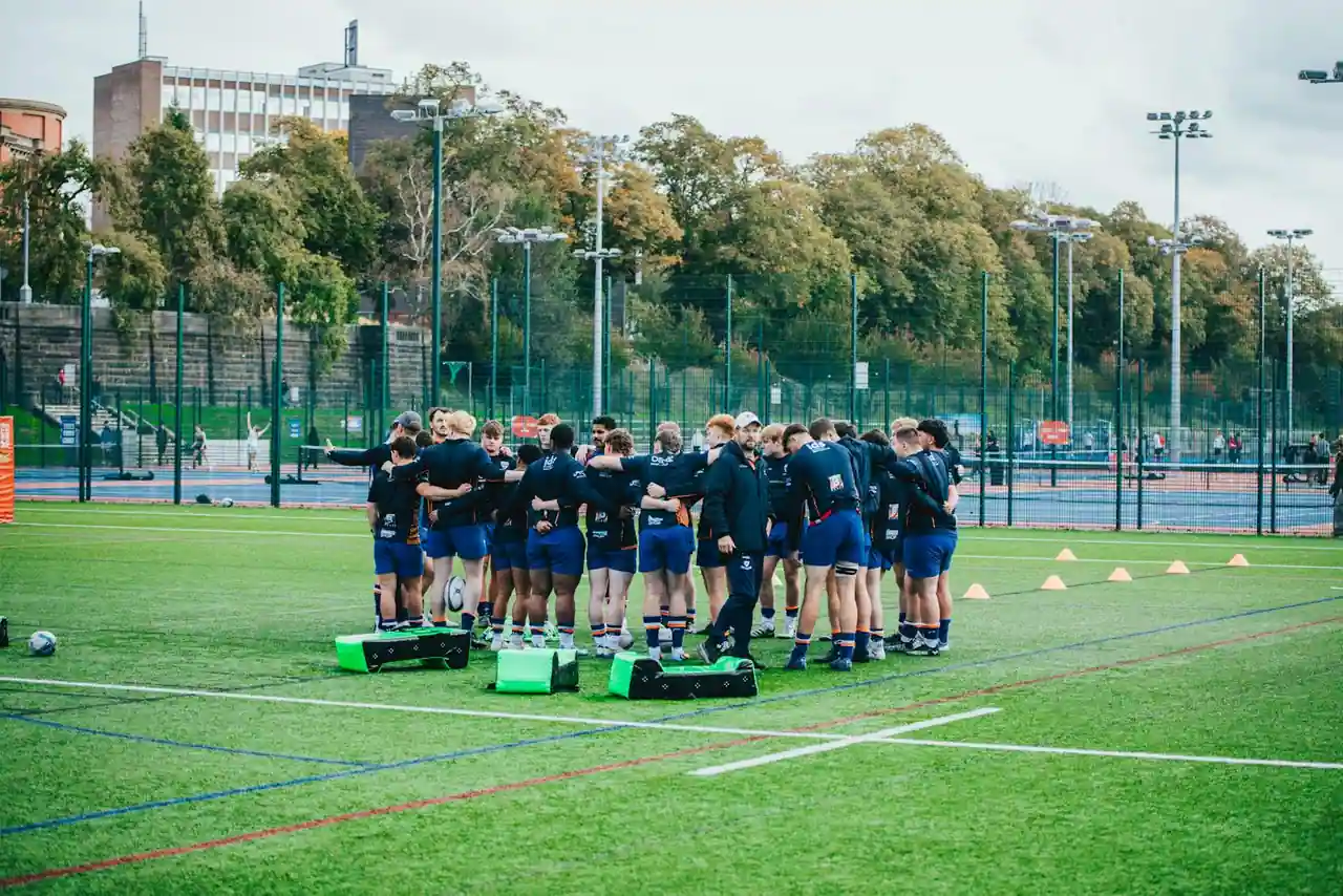Joueurs de rugby rassemblés en cercle sur la pelouse après un match, tête baissée