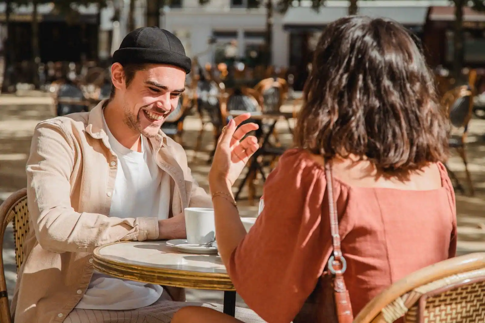 Un homme et une femme en conversation souriante à la terrasse d'un café, autour d'un café