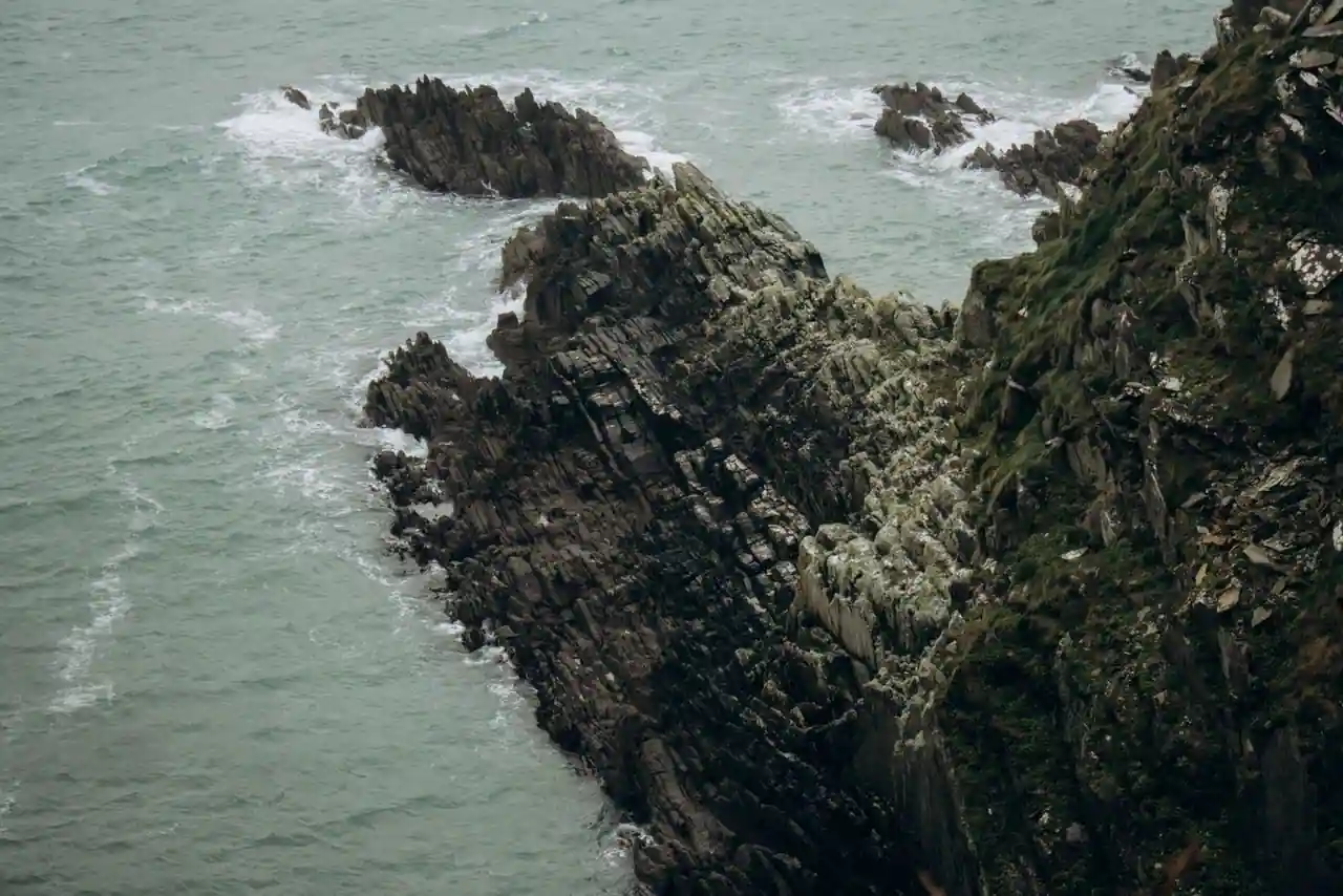 Côte rocheuse battue par le vent, rochers déchiquetés et lande au bord d'une mer écumante