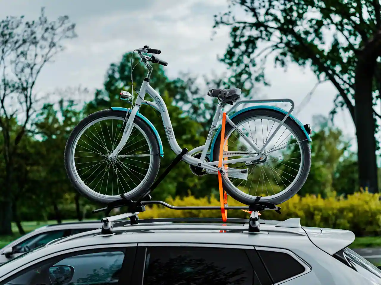 Vélo fixé sur un porte-vélos de toit, sanglé entre les barres transversales d'une voiture blanche.