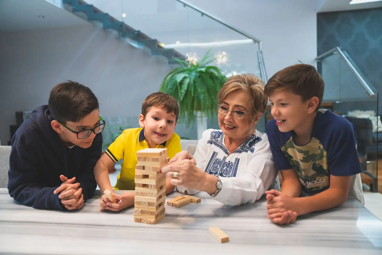 Une femme et trois enfants d'âges différents concentrés sur une tour de blocs en bois, autour d'une table