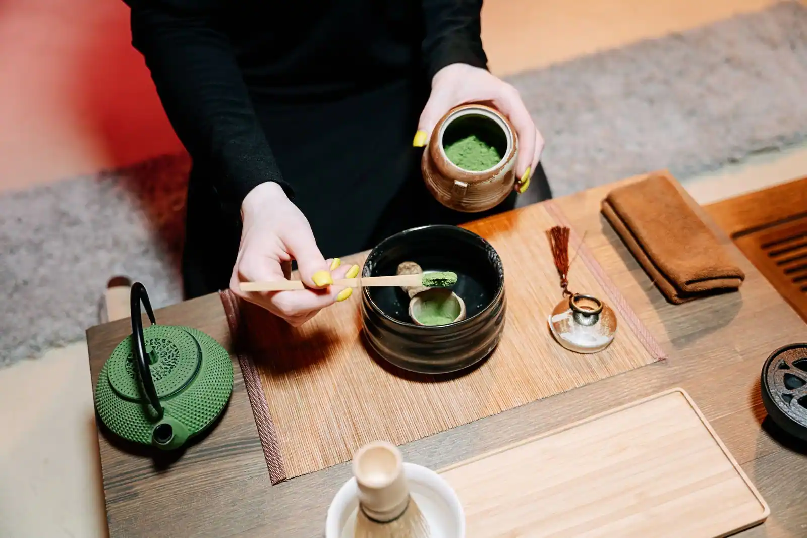Préparation du thé matcha : la poudre verte est déposée dans un bol noir, fouet en bambou à côté.