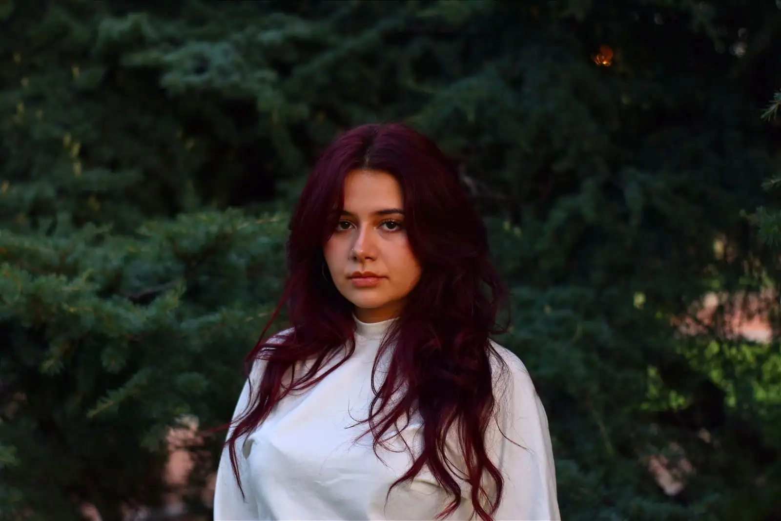 Une femme aux longs cheveux ondulés d'un brun-rouge profond, devant un feuillage sombre