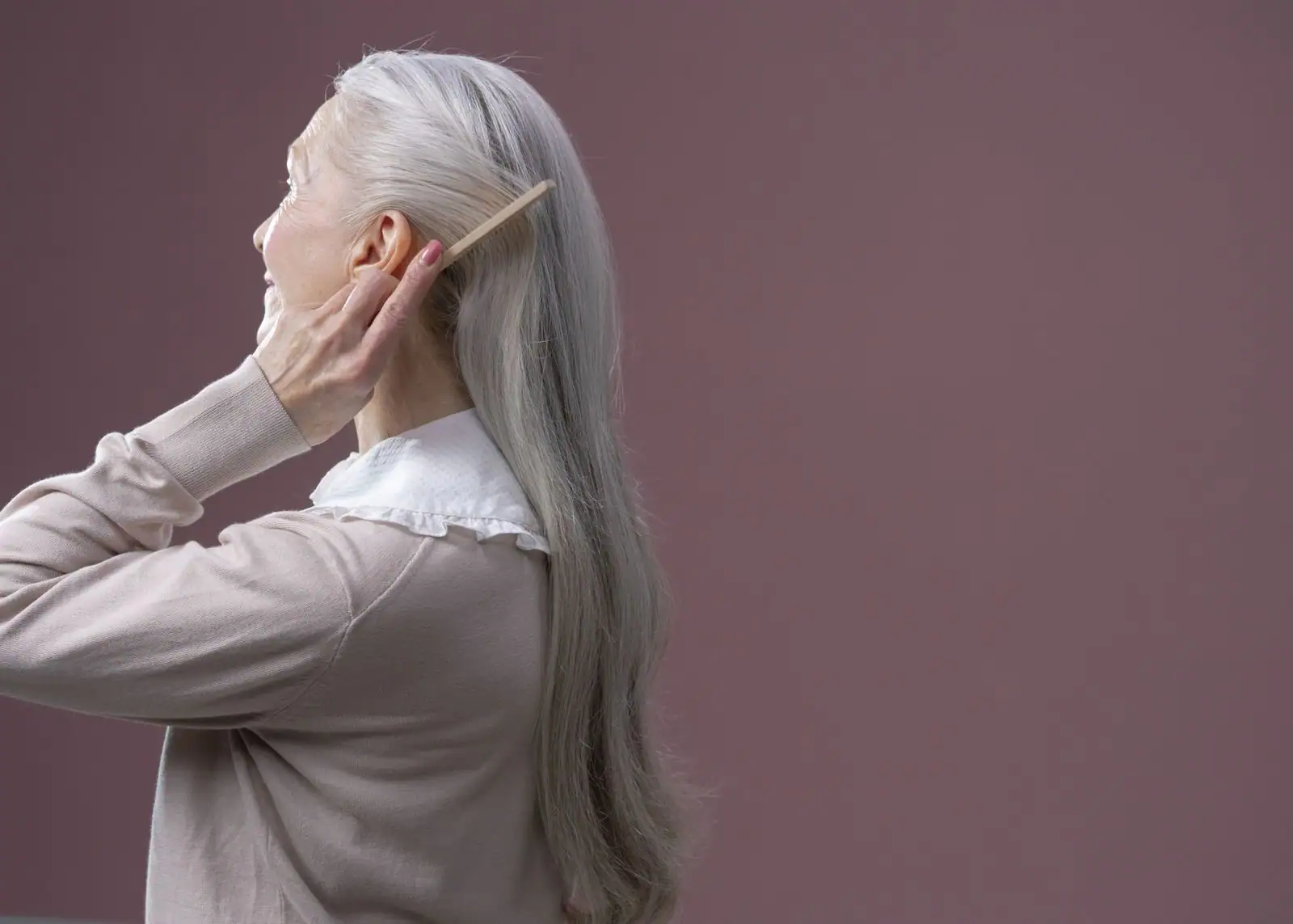 Femme âgée de profil aux longs cheveux argentés, se coiffant avec un peigne en bois.