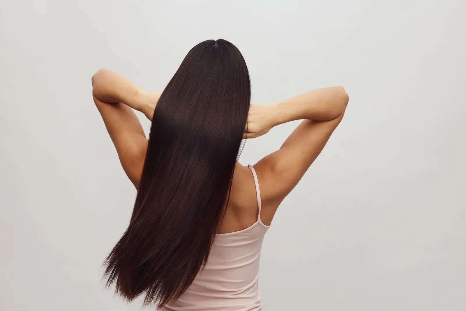 Femme de dos aux très longs cheveux bruns, parfaitement lisses et brillants, sur fond clair.