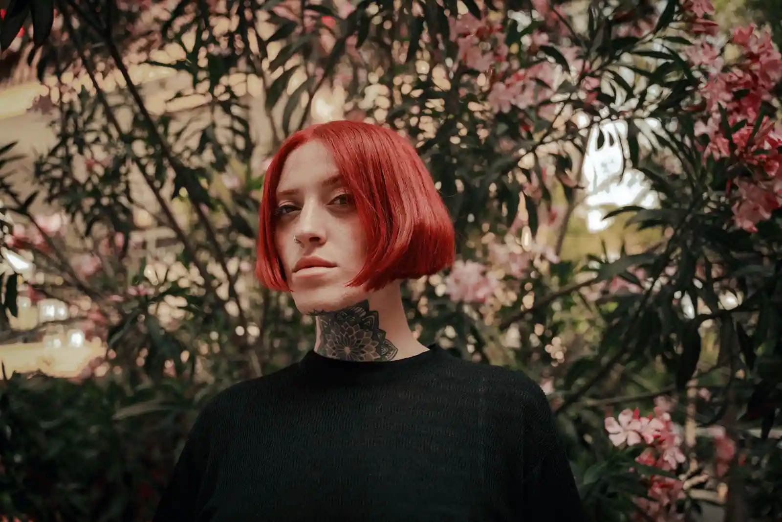 Coupe au carré teinte d'un rouge vif et brillant, portée par une femme devant un feuillage fleuri