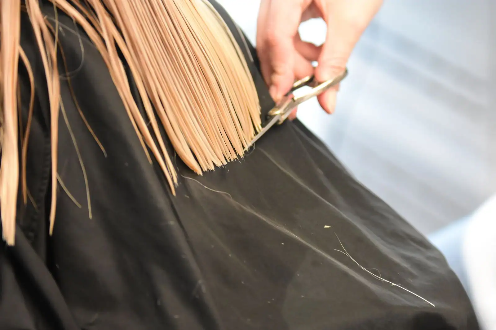 Gros plan sur une main tenant des ciseaux et coupant une mèche de cheveux blonds sur une cape noire