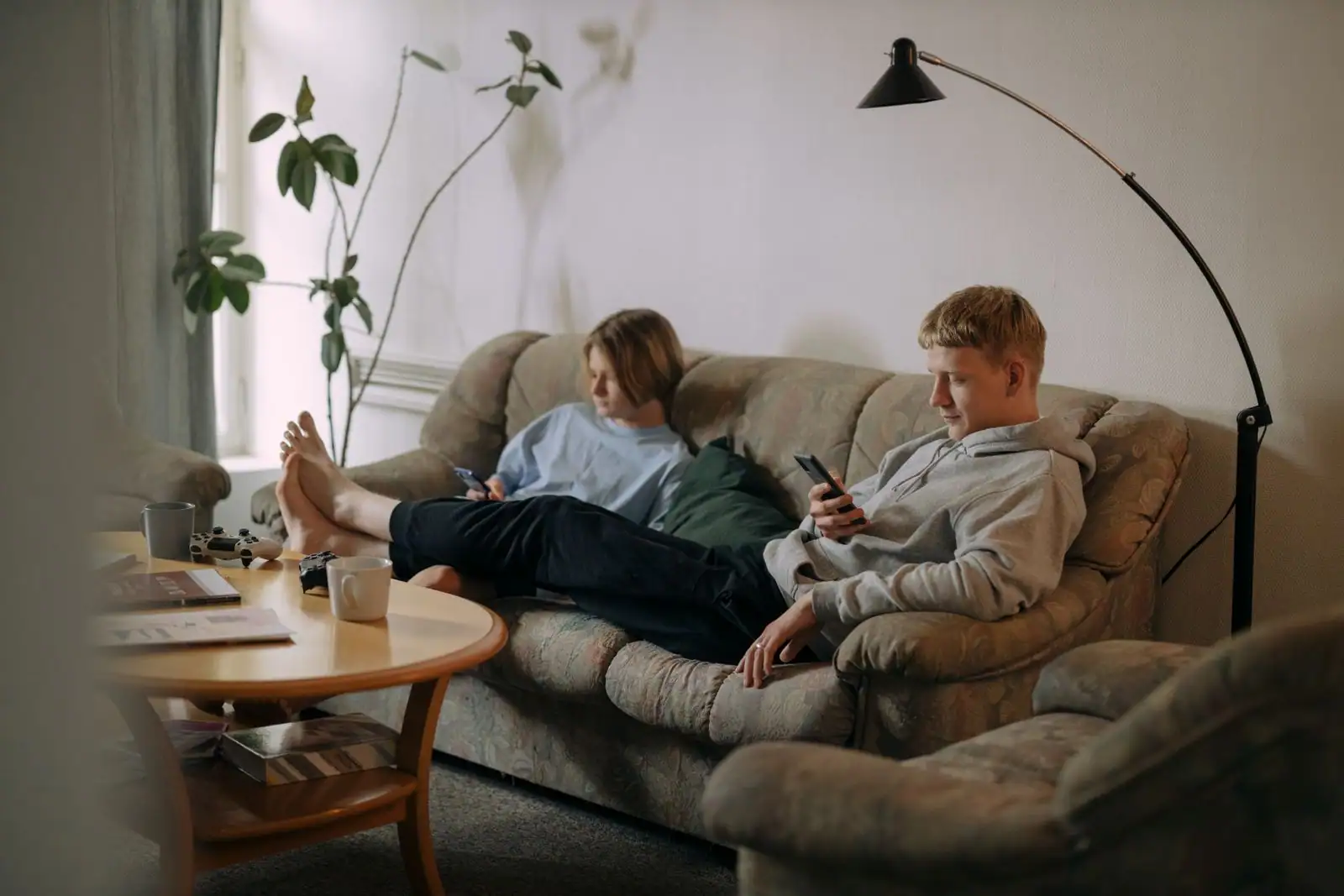 Couple assis sur un canapé, chacun absorbé par son téléphone, sans interaction, dans un salon.