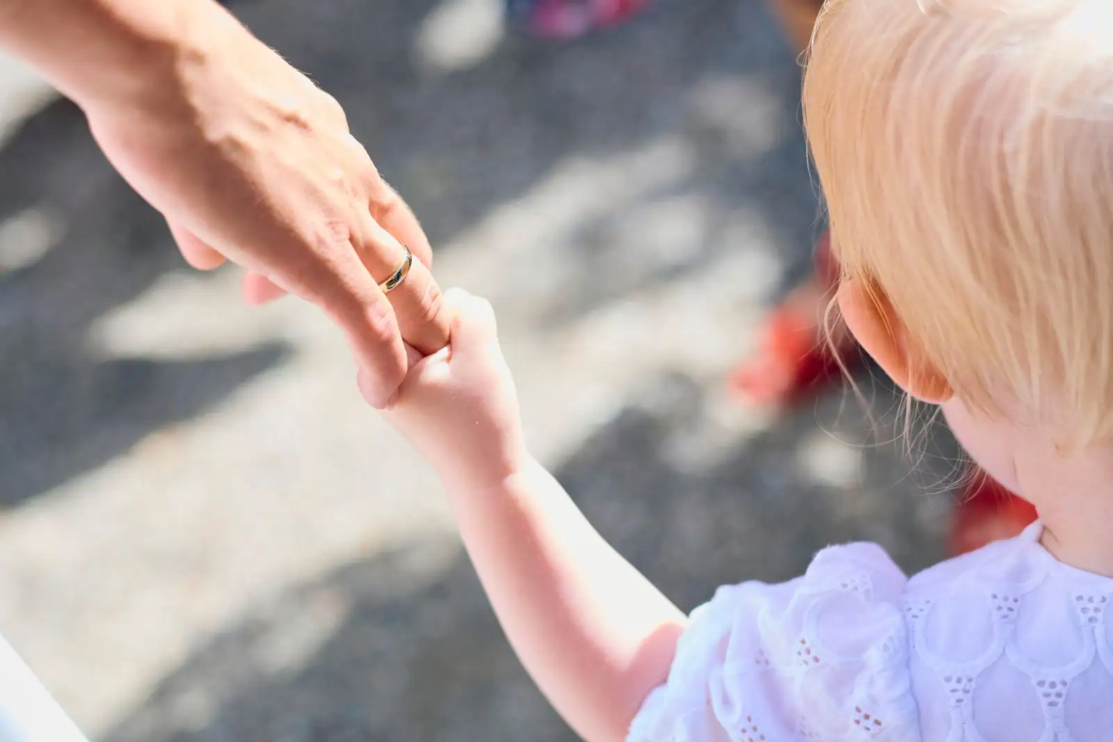 Gros plan sur la main d'un adulte tenue par celle d'un jeune enfant blond, dehors sur un trottoir
