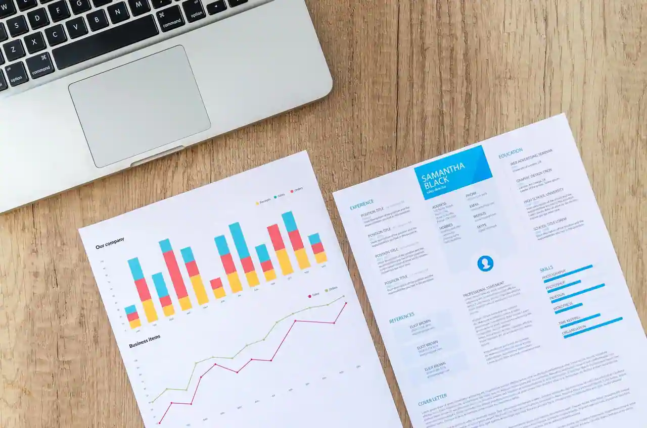 Un CV imprimé et une page de graphiques posés sur un bureau, à côté d'un ordinateur portable.