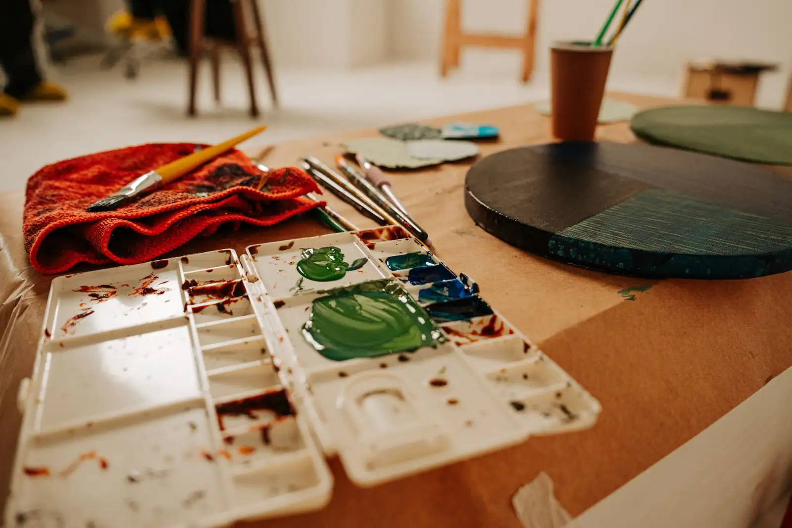 Palette de peinture maculée de vert, pinceaux et chiffon rouge posés sur une table couverte de kraft