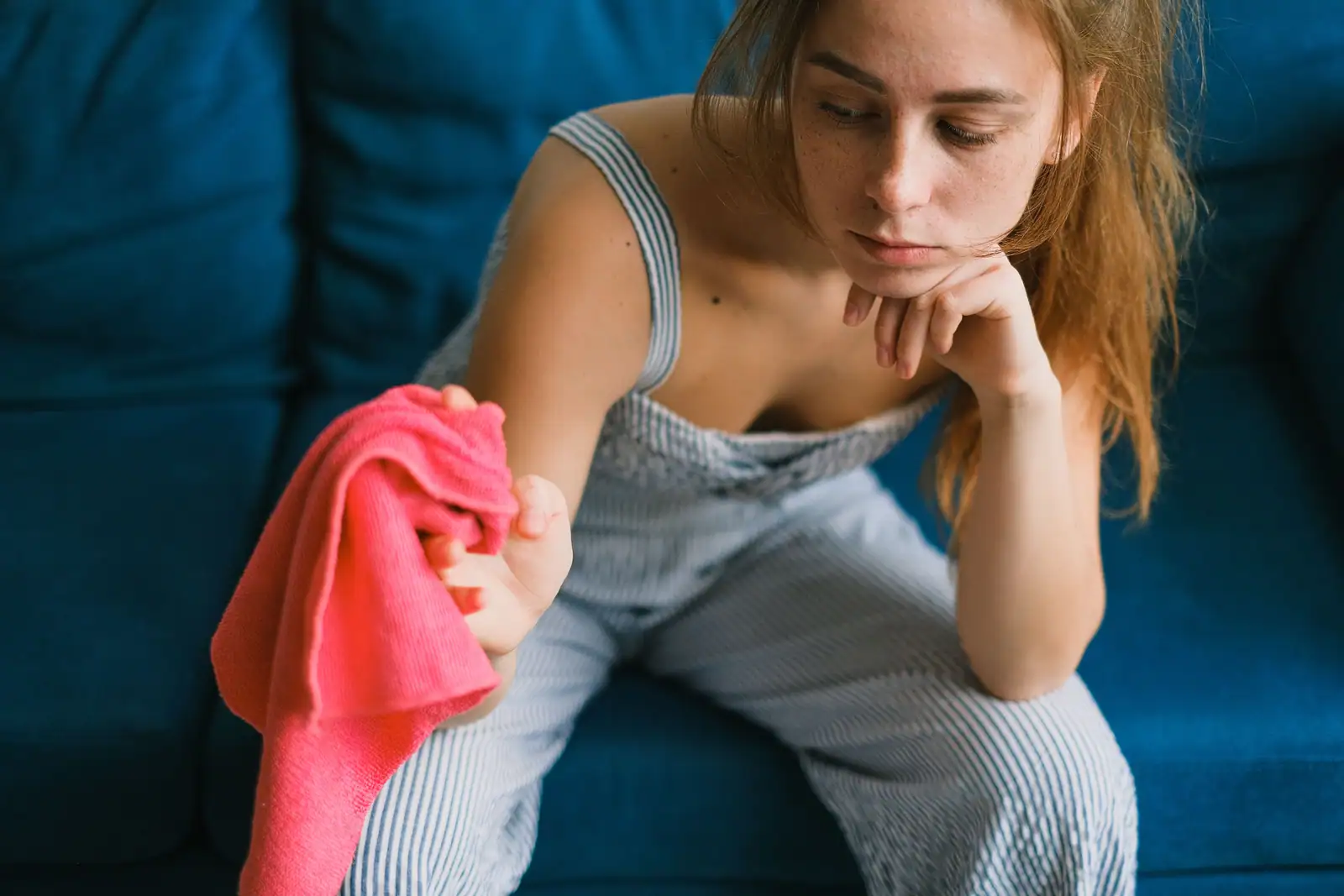 Image illustrative : femme assise sur un canapé, le menton dans la main, un chiffon de ménage à la main