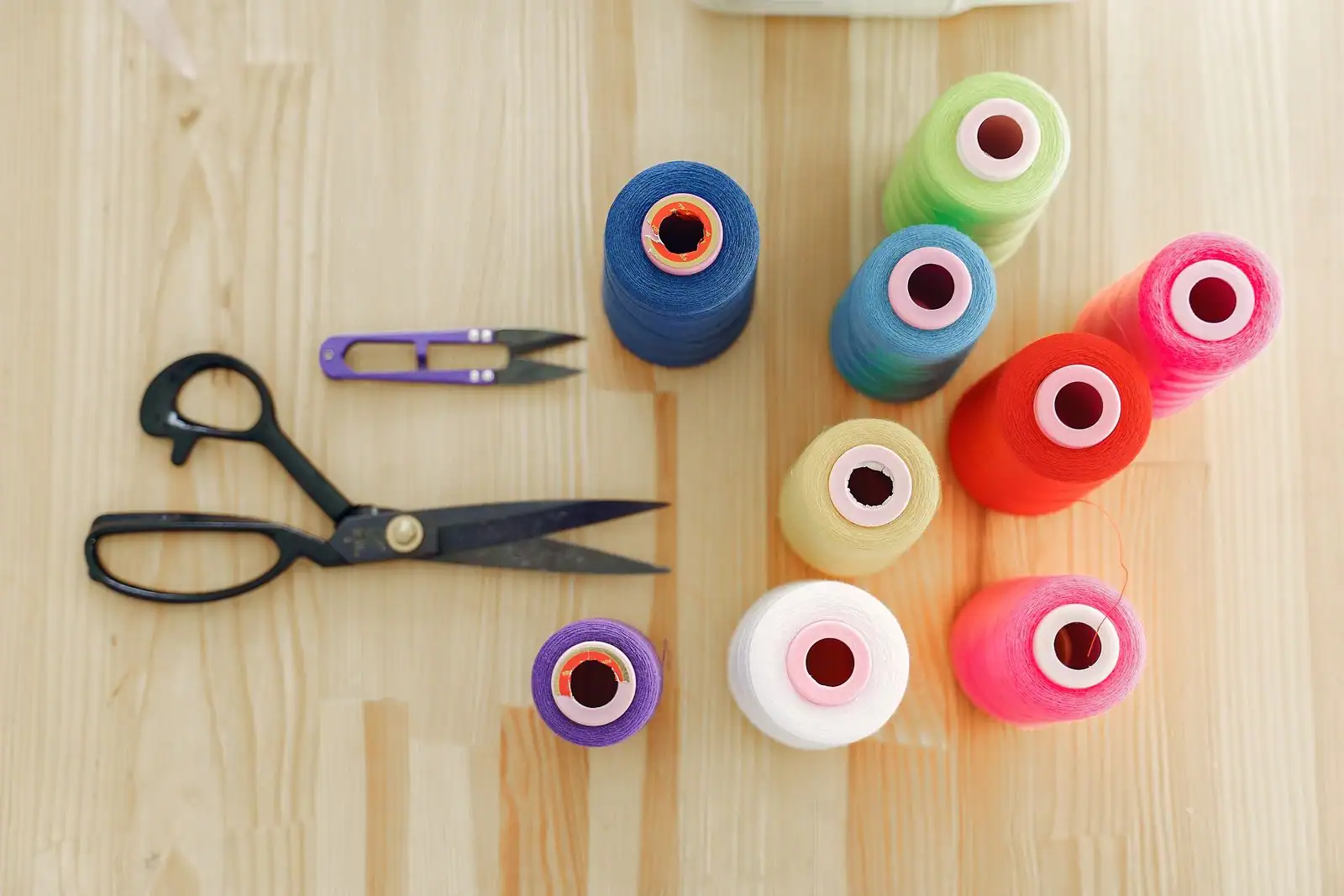 Bobines de fils colorés et ciseaux de couture posés sur une table d'atelier en bois.
