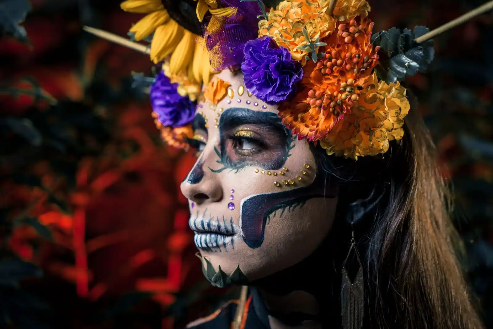 Maquillage de crâne fleuri sur une femme, orbites noires et dents tracées, couronne de fleurs orangées