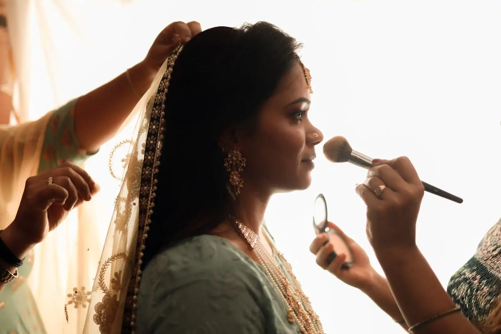 Maquillage d'une mariée appliqué au pinceau pendant sa préparation, voile et bijoux traditionnels