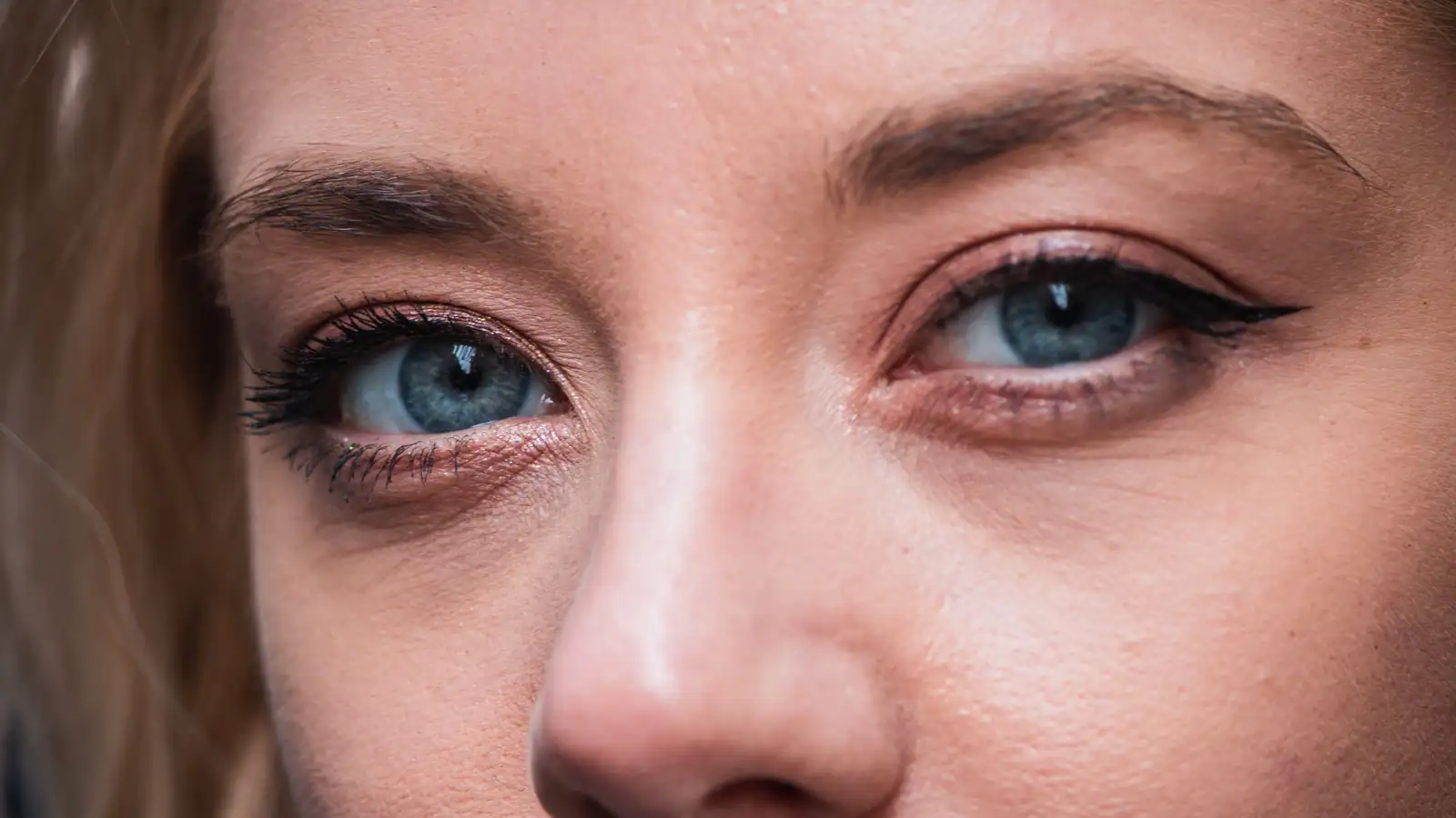 Gros plan sur les yeux bleus d'une femme, paupières fardées de rosé cuivré et trait noir