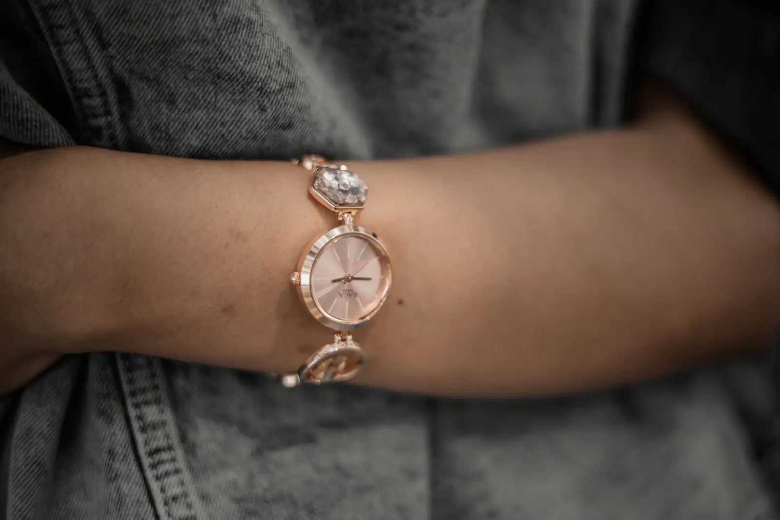 Montre-bracelet à petit boîtier doré rose et bracelet bijou, portée au poignet sur un vêtement en jean