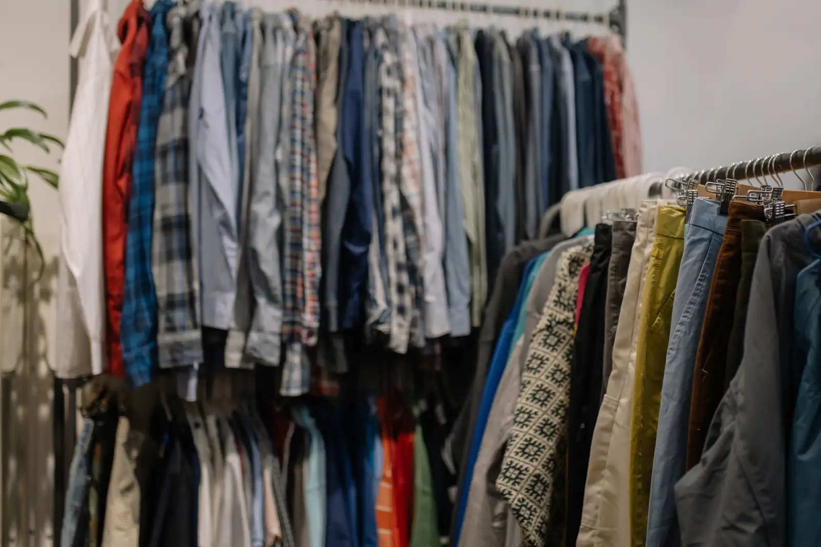 Portants densément garnis de vêtements variés dans une friperie : chemises, vestes et pantalons.