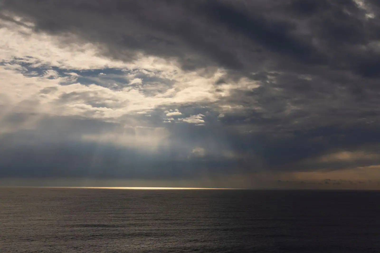 Épaisse couche nuageuse au-dessus de l'océan, percée de rayons de lumière jusqu'à l'horizon.