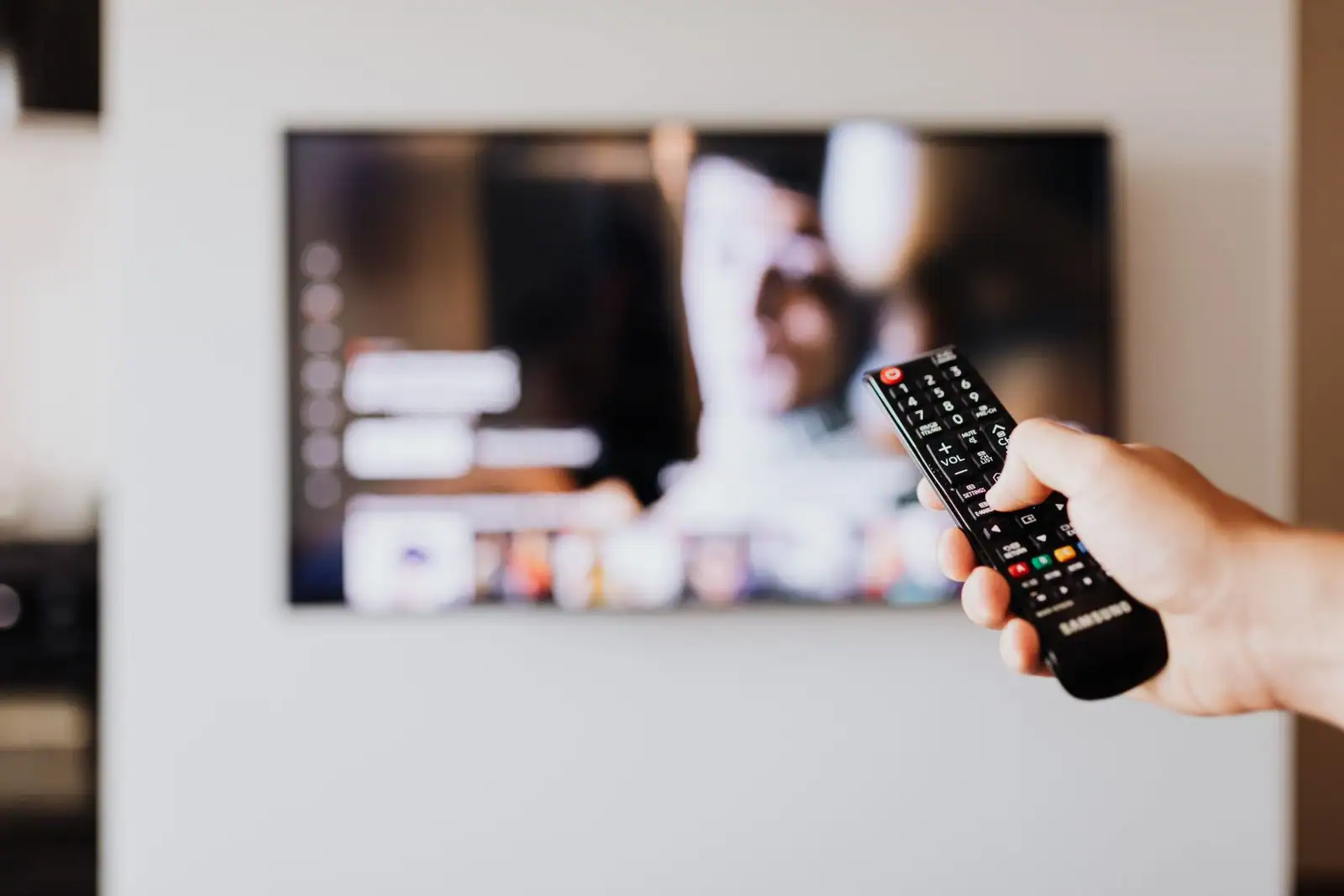 Une main pointe une télécommande vers un téléviseur affichant son menu à l'écran.