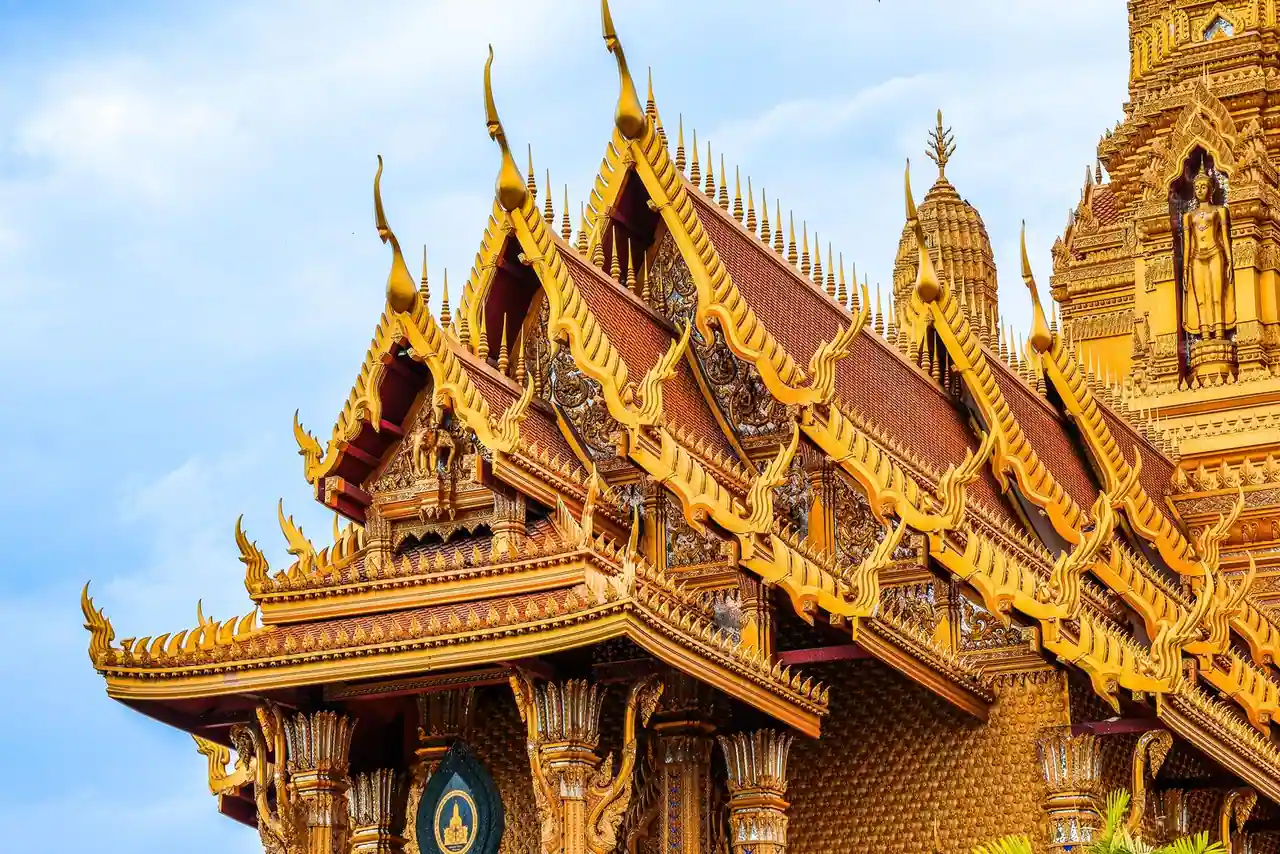 Temple bouddhiste thaïlandais aux toits dorés et ornements traditionnels sous un ciel clair