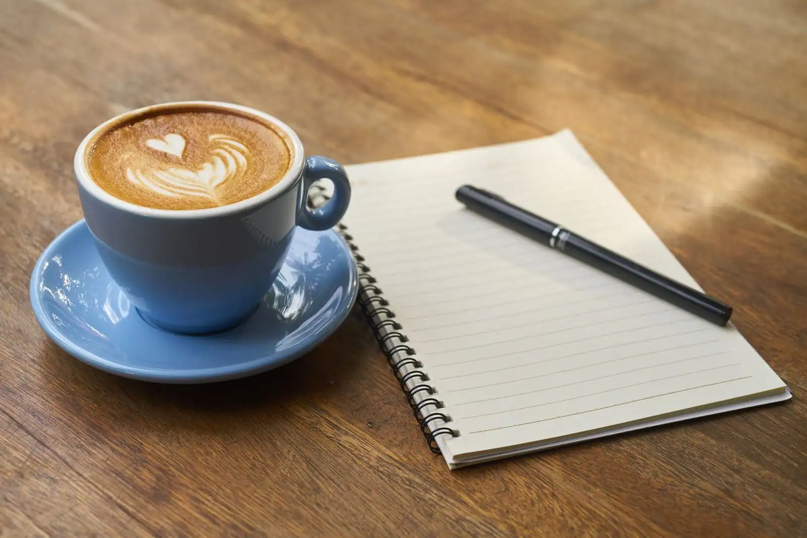 Carnet ouvert avec un stylo posé à côté d'une tasse de café sur une table en bois.