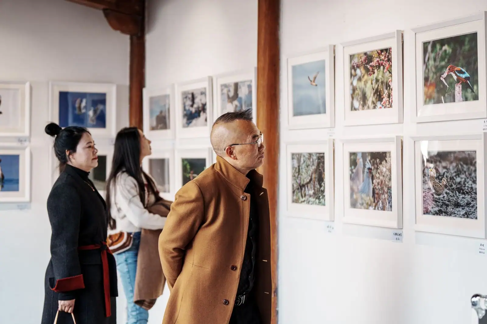Visiteurs observant des photographies encadrées lors d'une exposition dans une salle lumineuse
