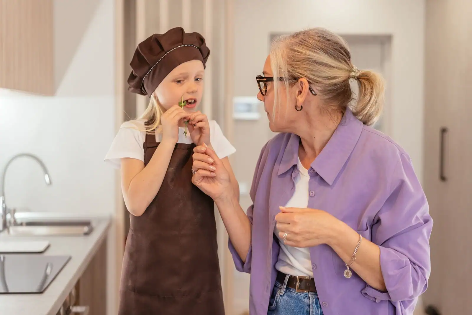 Deux générations dans une cuisine : une femme âgée et une enfant coiffée d'une toque de cuisinier