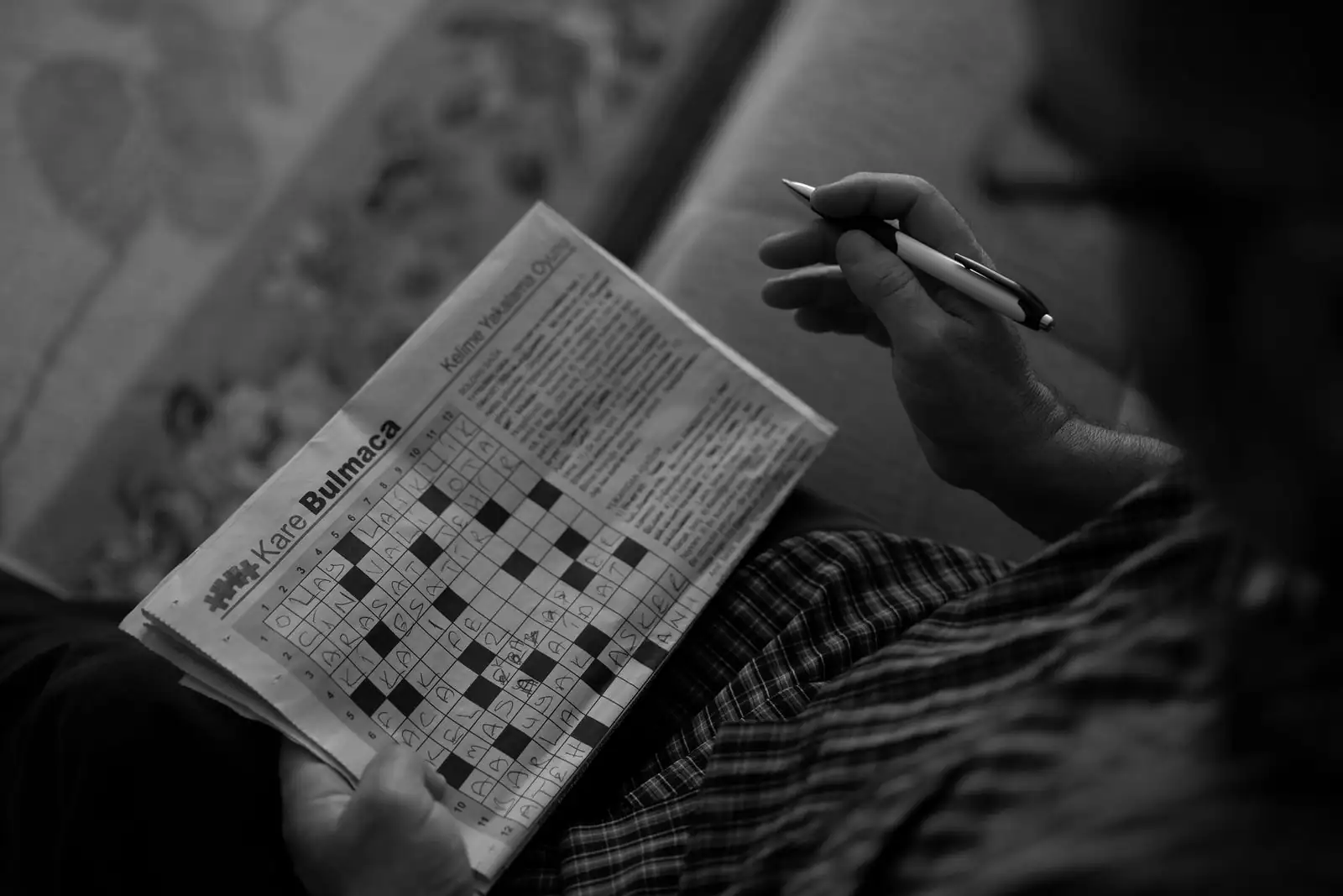 Une personne remplit une grille de mots croisés dans un magazine de jeux, un stylo à la main.