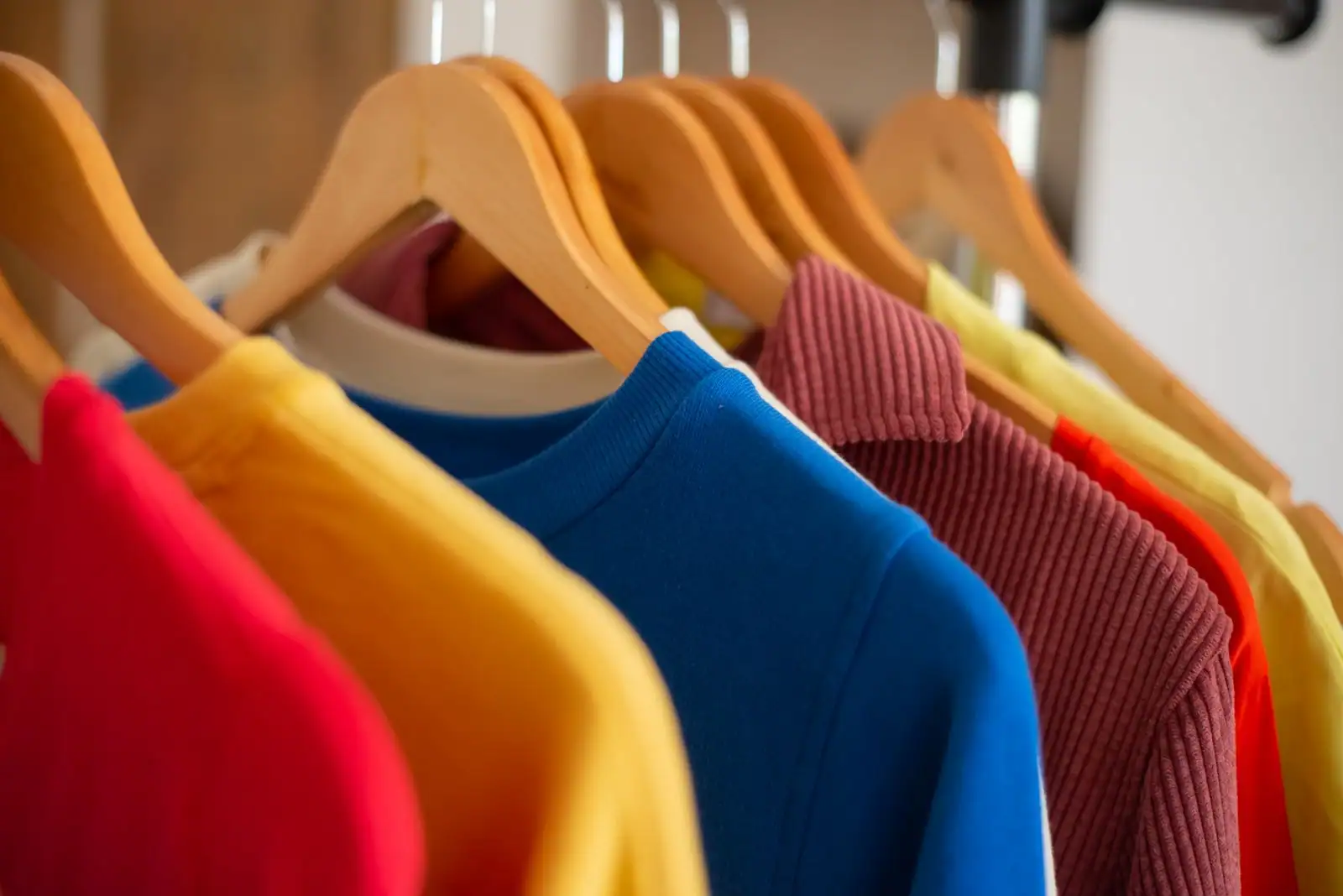 Hauts en maille colorés suspendus sur des cintres en bois le long d'un portant de vêtements