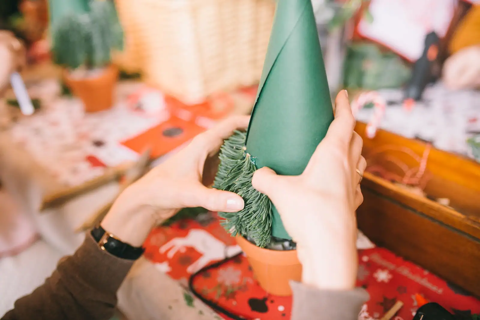 Mains fabriquant un petit sapin de Noël en papier vert sur une table décorée en rouge