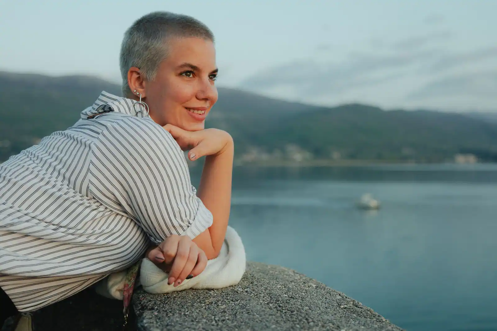Femme au crâne rasé très court, sourire, vue côtière en arrière-plan