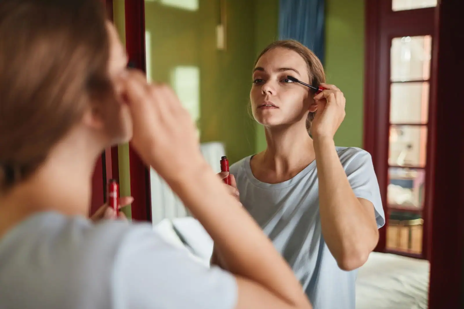 Jeune femme réalisant un maquillage léger et naturel devant un miroir de salle de bain