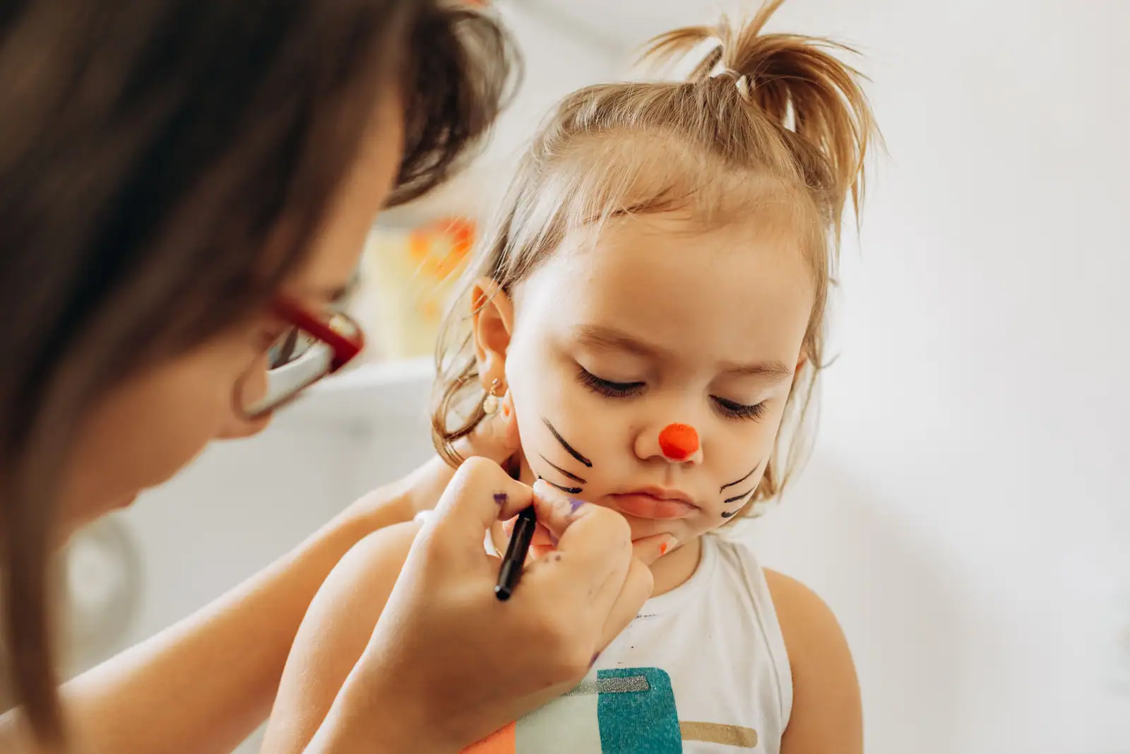 Enfant avec un maquillage de lapin peint sur le visage, nez rose et moustaches dessinées.